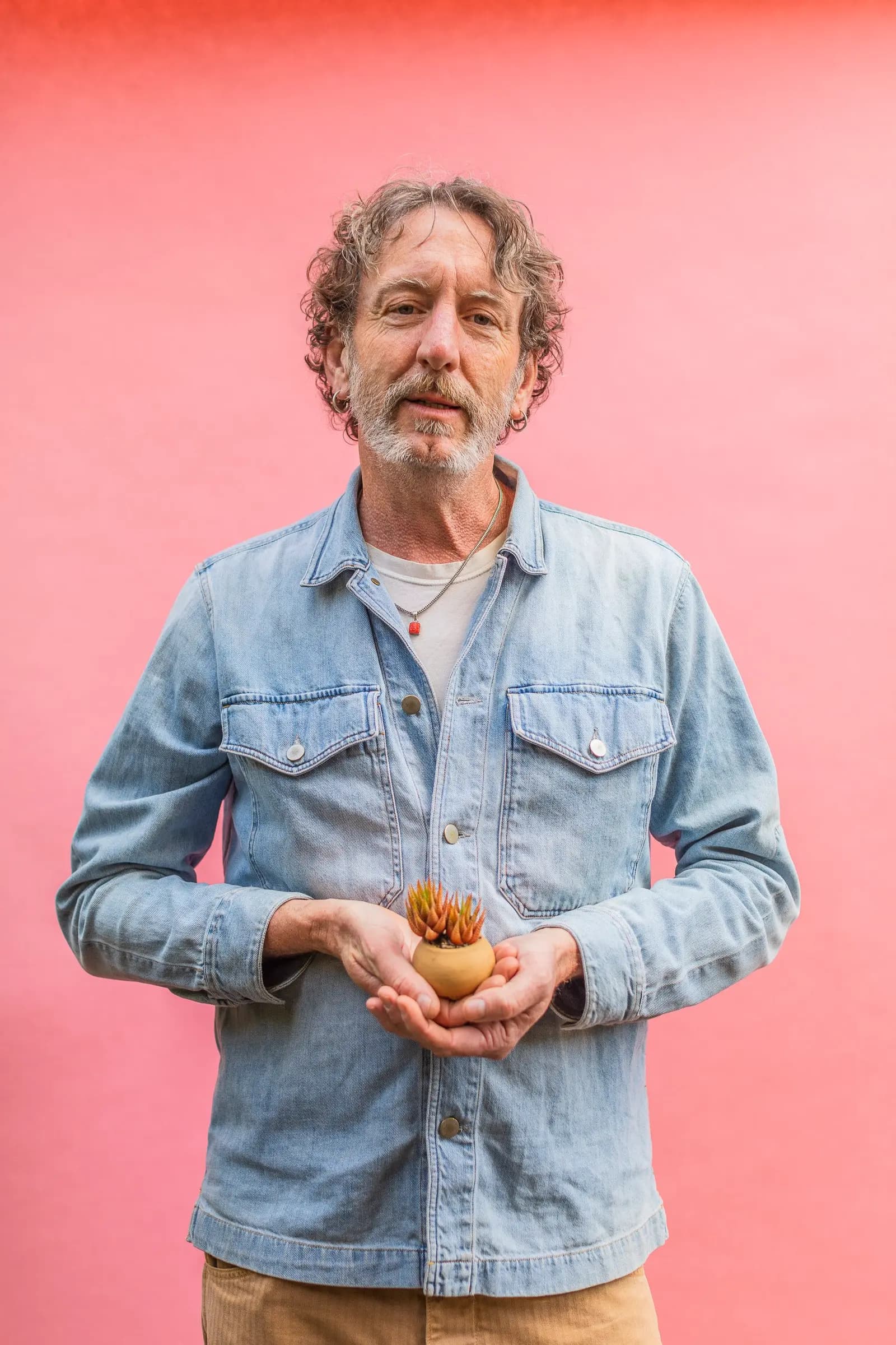 Clarke de Mornay, miembro del equipo de Flora Grubb Gardens desde hace años, sostiene una pequeña maceta de barro con suculentas frente a un fondo rosa.