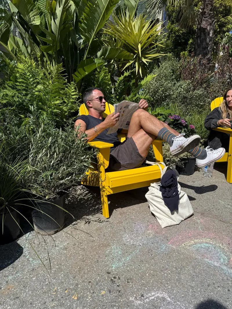 Manny Yekutiel, con lentes de sol, descansa en una banca amarillo brillante en la plaza pop-up de Cole Valley de Flora Grubb Gardens y la Civic Joy Foundation.
