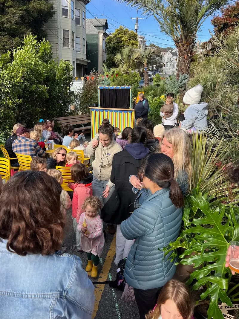 Niños y adultos reunidos al aire libre en un pequeño espectáculo de títeres en la plaza pop-up de Cole Valley creada por Flora Grubb y la Civic Joy Foundation.