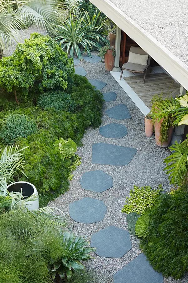 El jardín de la casa de Flora Grubb con un camino de piedras, acacia Cousin Itt y una zona para sentarse bajo un patio techado.
